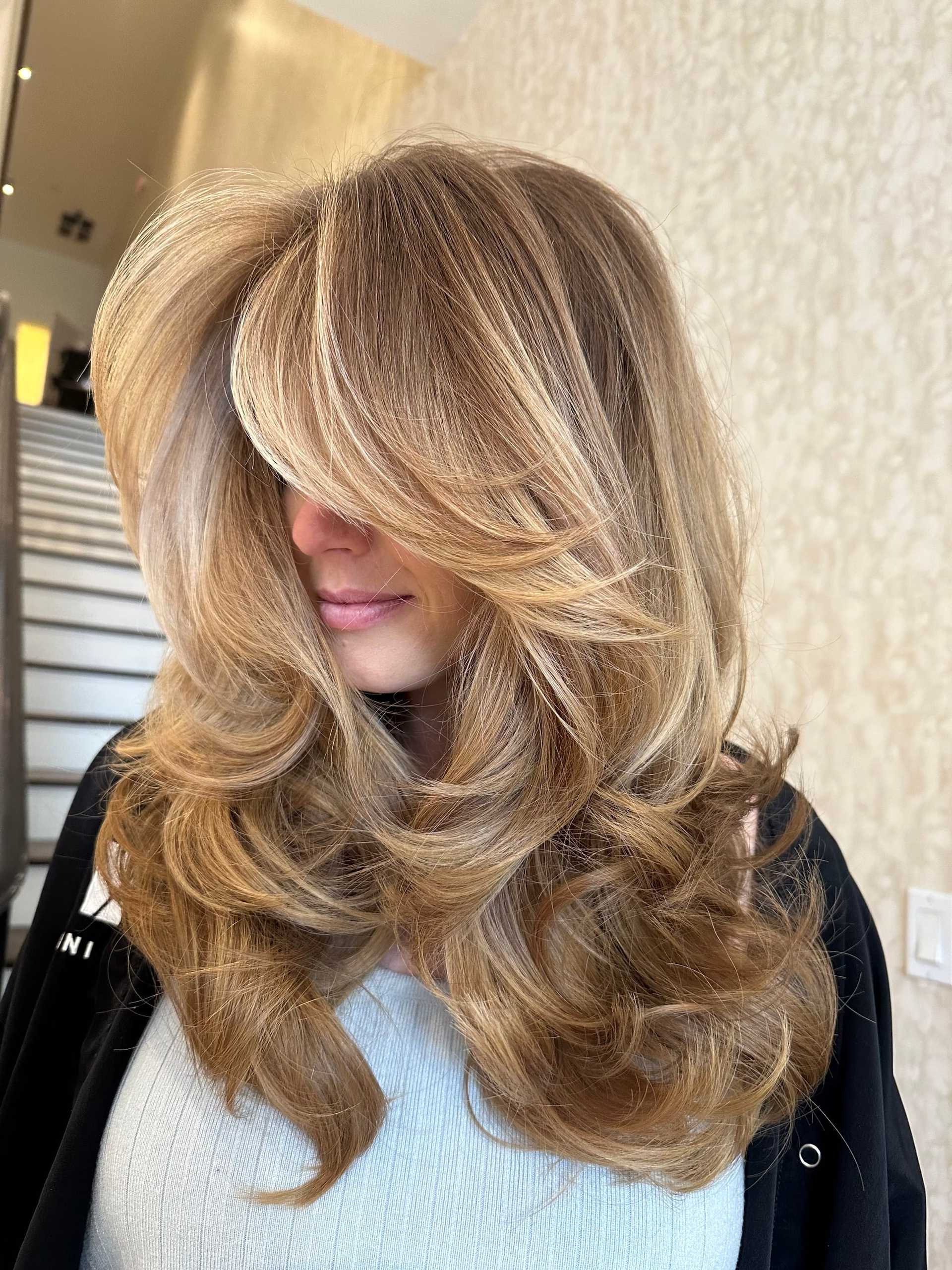 Long, wavy blonde hair with highlights, styled for volume in a salon setting.