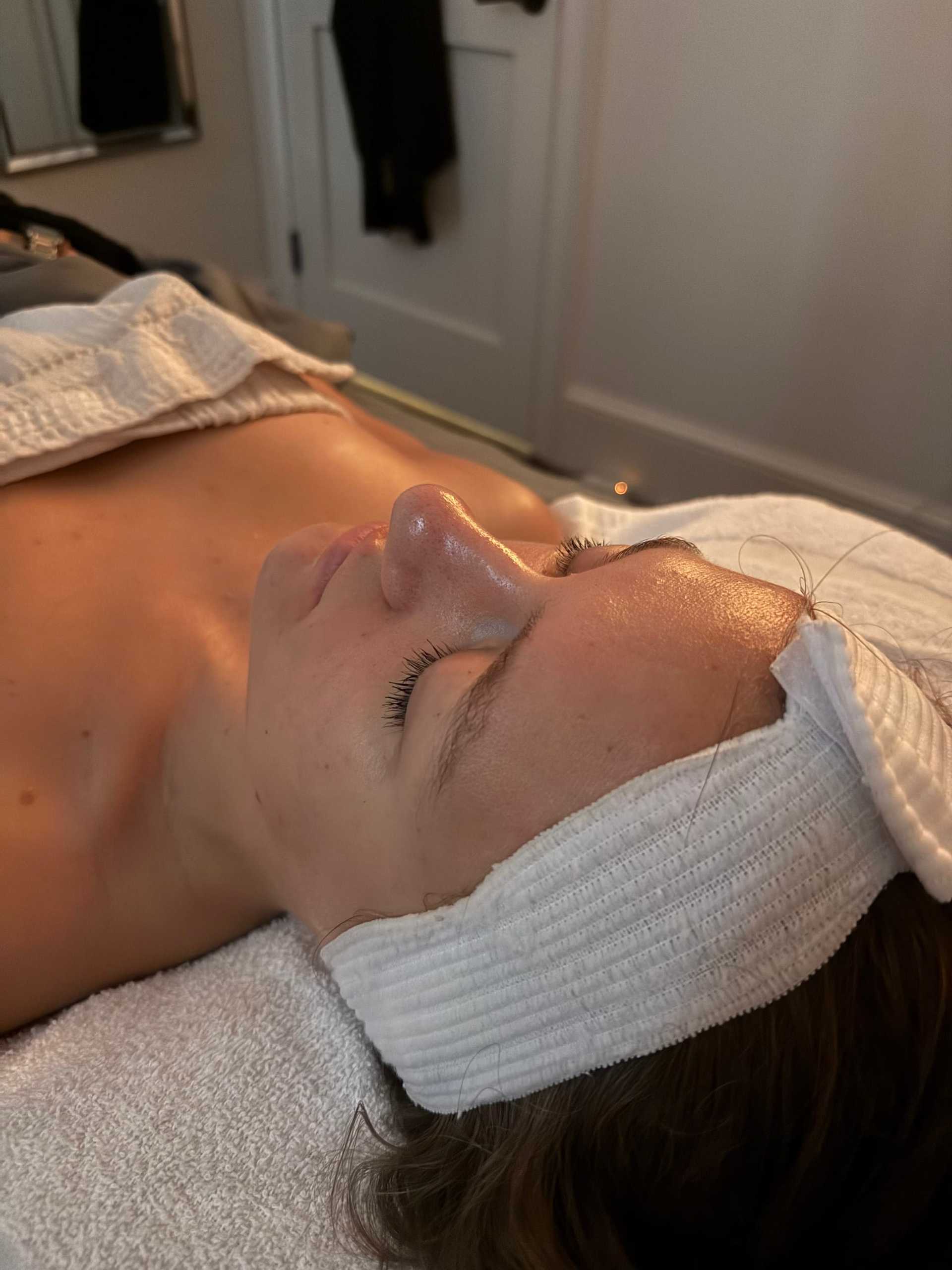 Person resting during a spa facial treatment, wearing a headband and covered with a towel.