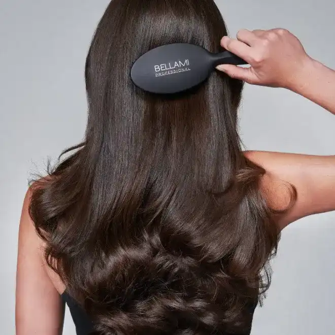 Woman brushing long, wavy brown hair with Bellami brush.